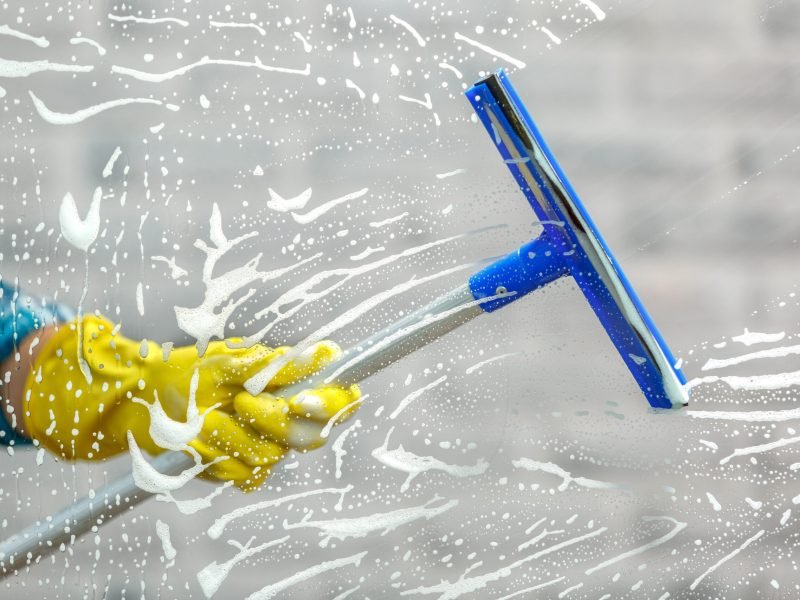 Studio shot through glass of housekeeper. Woman hand with glove holding squeegee for window. Focus on hand