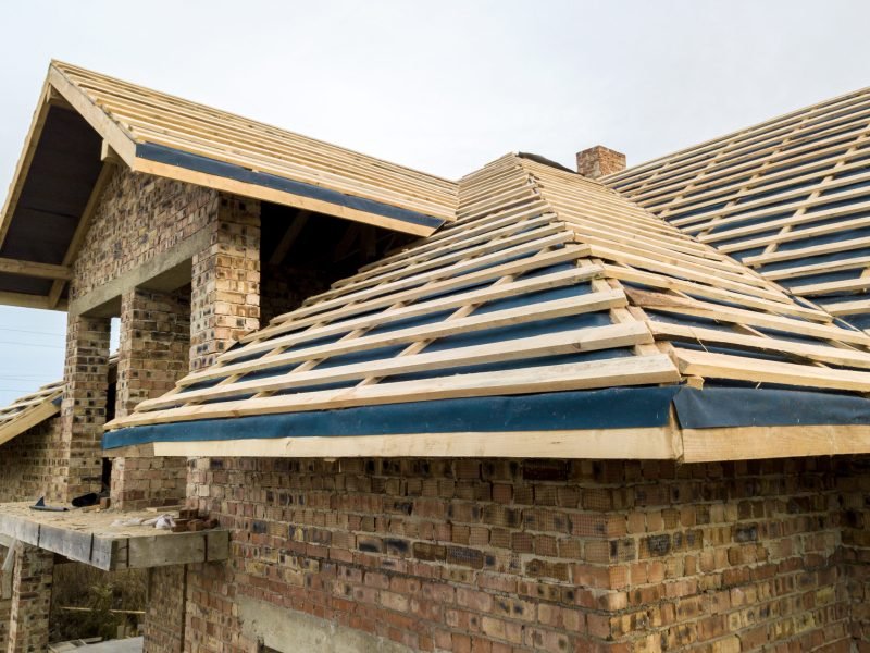 Private residential house with wooden roof frame structure under construction. Unfinished brick building under development.